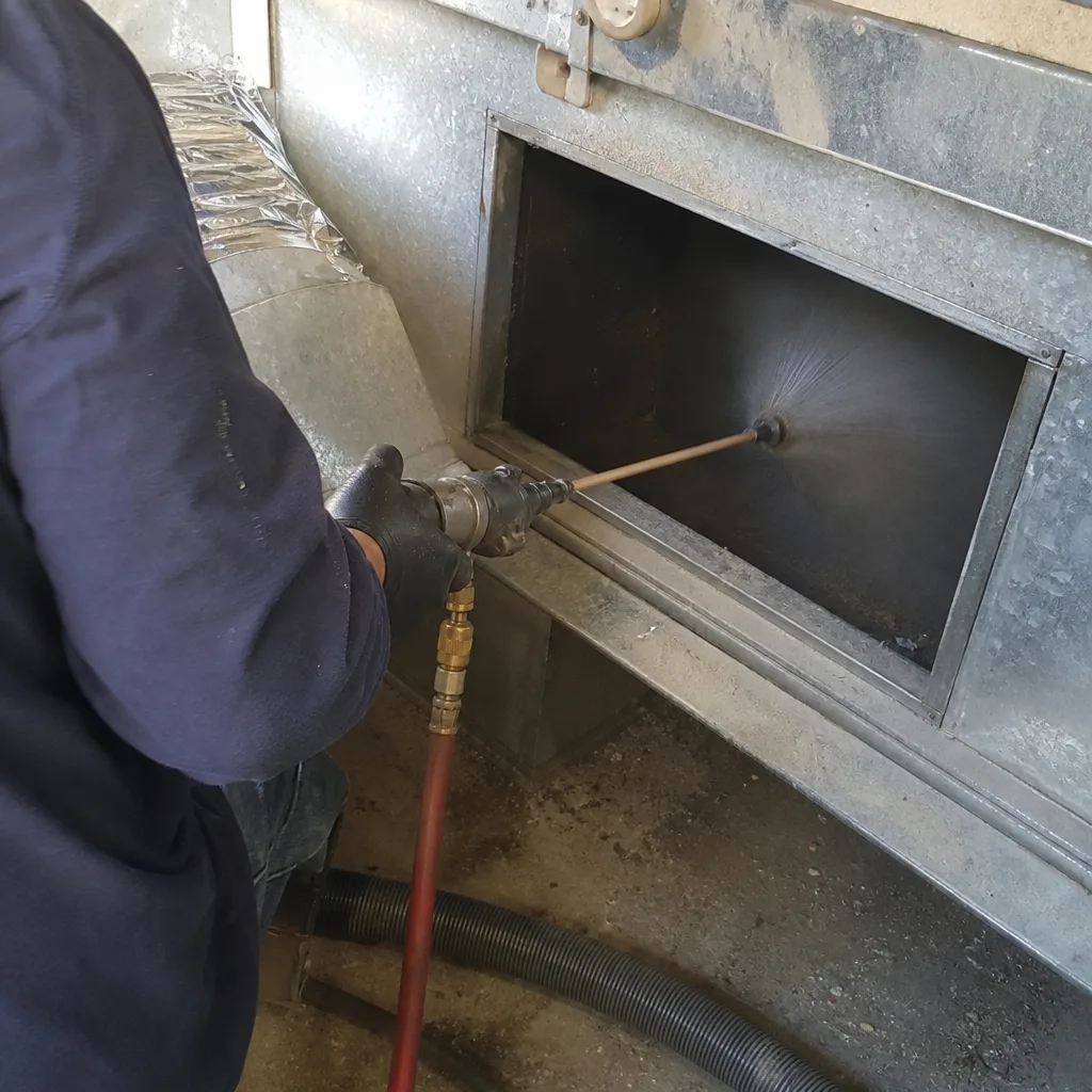 Technician performing professional air duct cleaning with specialized spray equipment